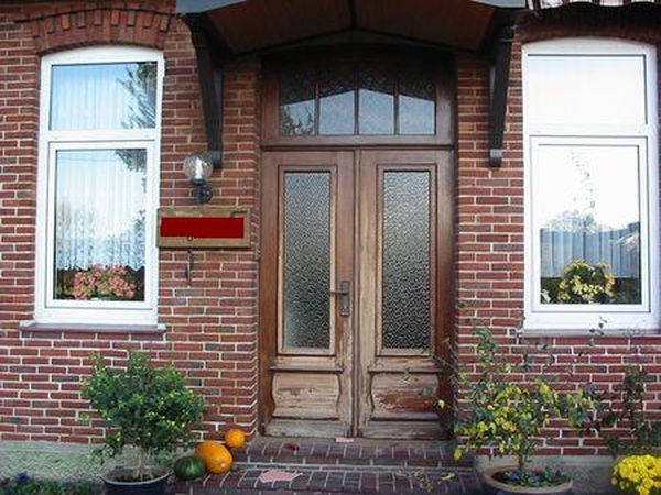 Alte verwitterte Holzhaustür mit abblätterndem Lack an einem Backsteinhaus vor der Renovierung